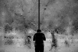 Silhouette of a person wearing a backpack standing in front of a foggy, textured glass panel.