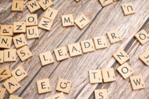 Scrabble tiles on a wooden table spelling the word 'LEADER'.